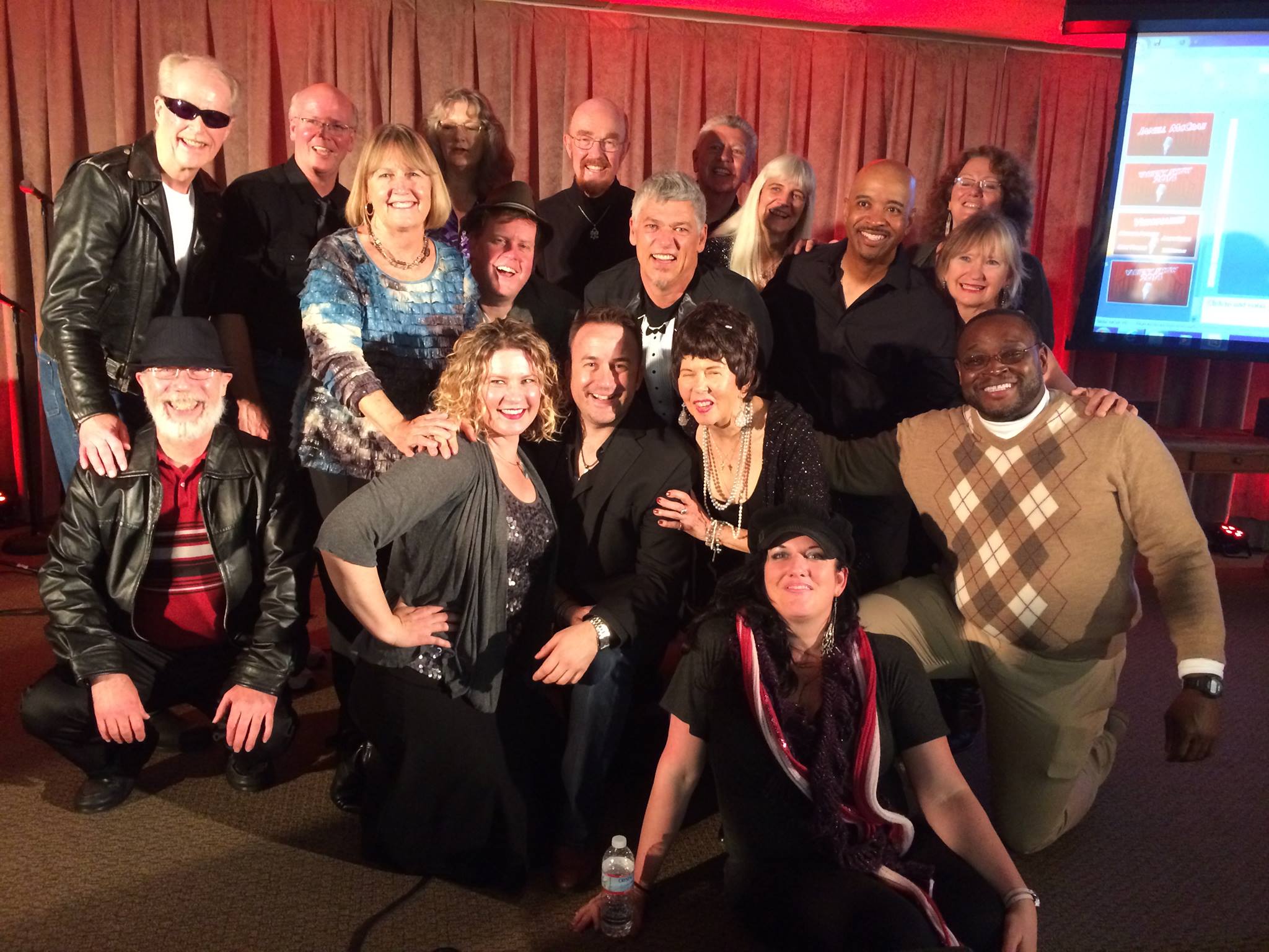 A large group of people smiling and posing together indoors with a curtain backdrop. A large group of people smiling and posing together indoors with a curtain backdrop.