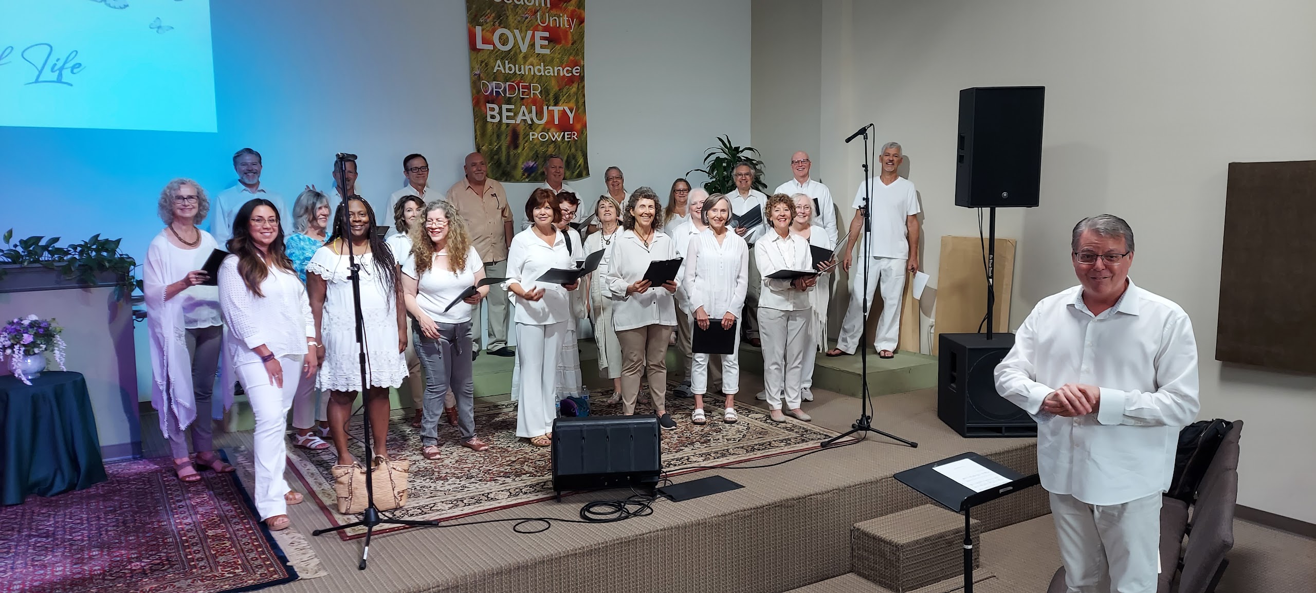 A choir group dressed in white performing on stage with their conductor.