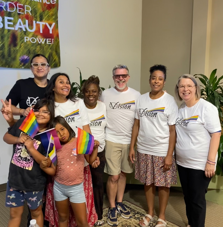 Diverse group smiling, holding pride flags, wearing matching ‘Vision’ shirts. Diverse group smiling, holding pride flags, wearing matching 'Vision' shirts.