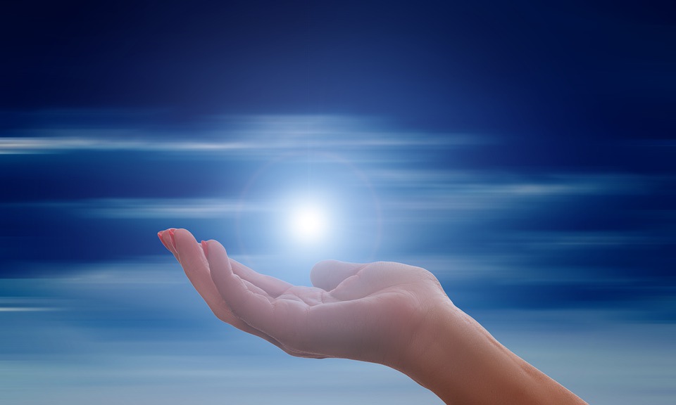 A hand reaching out towards a glowing light in a blue sky.